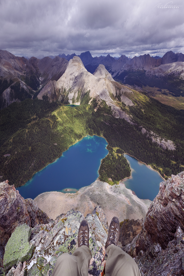 A first person perspective of feet hanging off the summit of Sunburst Peak with Sunburst lake and Cerulean lake way down below.